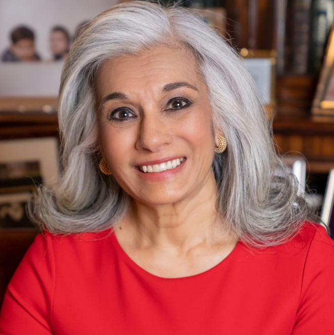 Portrait of HRH Princess Sarvath El Hassan smiling, wearing a red top, in a library setting